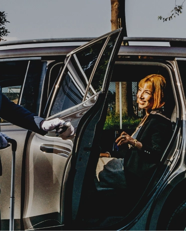 Professional chauffeur in suit and gloves opening the door of an executive SUV for a smiling business traveler in Colombia.