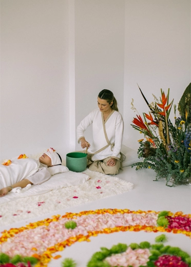 Terapista che suona una campana tibetana accanto a un mandala di fiori durante un rituale di guarigione in Colombia