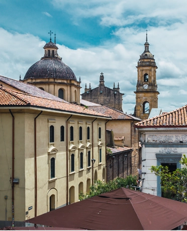 La Candelaria historic district in Bogotá with the dome and bell tower of the Primada Cathedral against the Andes sky.