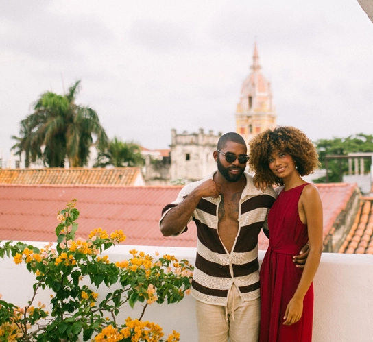Couple posing on a Cartagena rooftop with bougainvillea flowers and colonial domes of the historic center in the background.