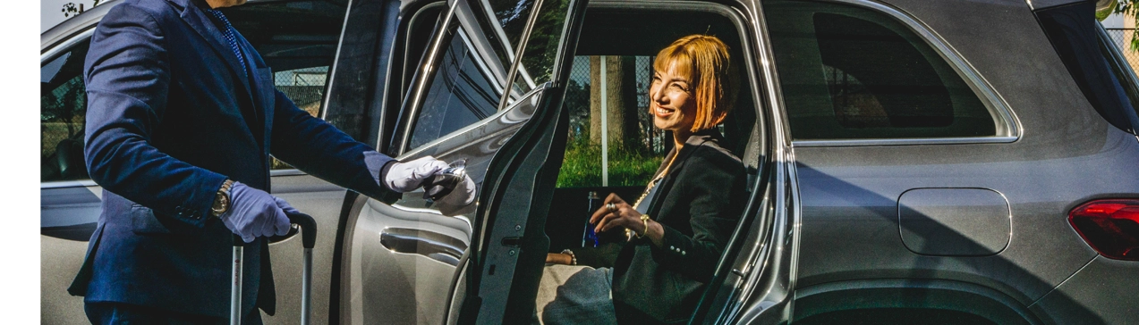 Professional chauffeur in suit and gloves opening the door of an executive SUV for a smiling business traveler in Colombia.
